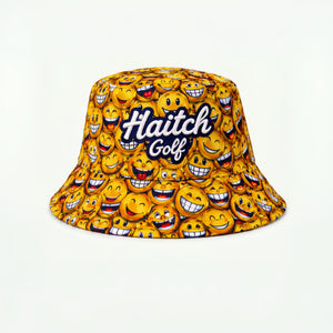 A yellow bucket hat featuring an all-over pattern of smiling emoji faces and the text 'Haitch Golf' in white script with a dark blue outline, set against a plain white background.