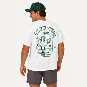 A man wearing a white short-sleeve t-shirt with a green graphic on the back, paired with dark gray shorts and a green baseball cap, shown from a rear three-quarter view against a plain white background.