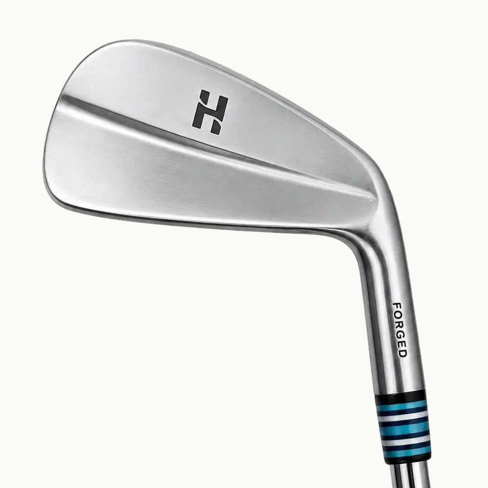 A close-up studio shot of a Haitch Golf Marksman MB iron golf club head and part of the shaft on a light off-white background, with product text below.